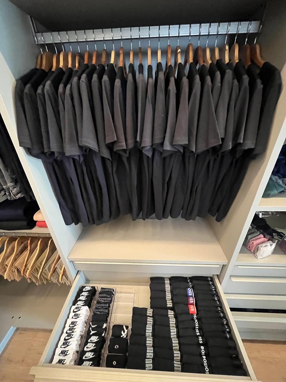 Closet organizado, com camisetas e polos pendurados por cor e gaveta de meias dobradas em pares